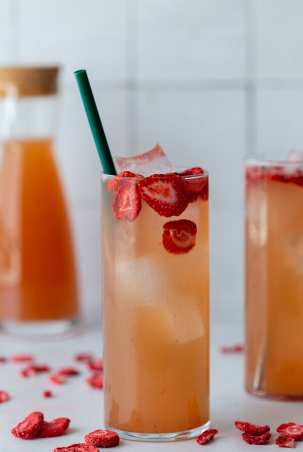 tall glass filled with a pink drink, ice, and strawberries