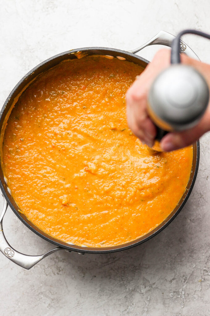 Using an immersion blender to make orange soup creamy.