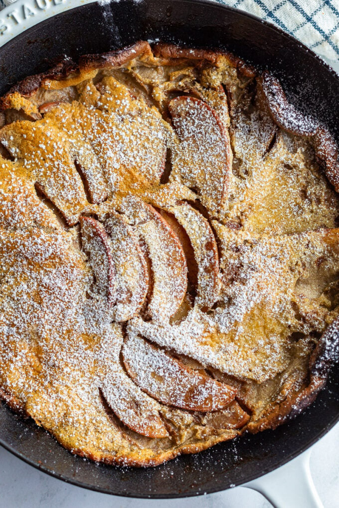 up close shot of an apple dutch baby in a cast iron skillet. Dusted with powdered sugar