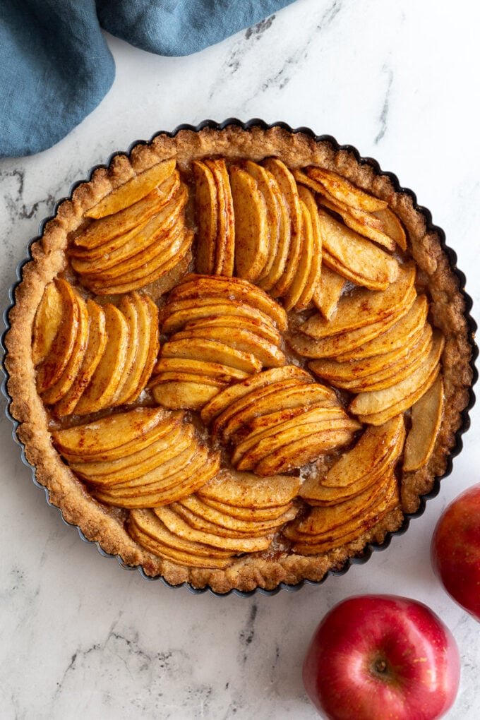 Baked apple tart on a marble board. The tart has apple arranged in groups that are going in different directions