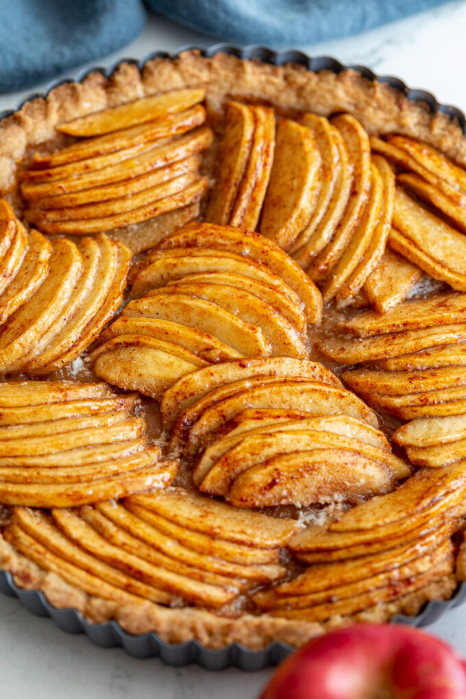 side shot of a baked apple tart on a marble board. The tart has apple arranged in groups that are going in different directions