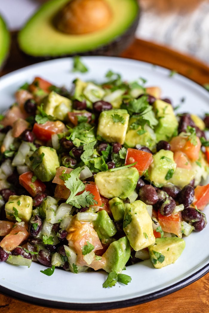 side shot of a tin bowl filled with avocado and black bean salad with tomato, onion and cilantro mixed in as well