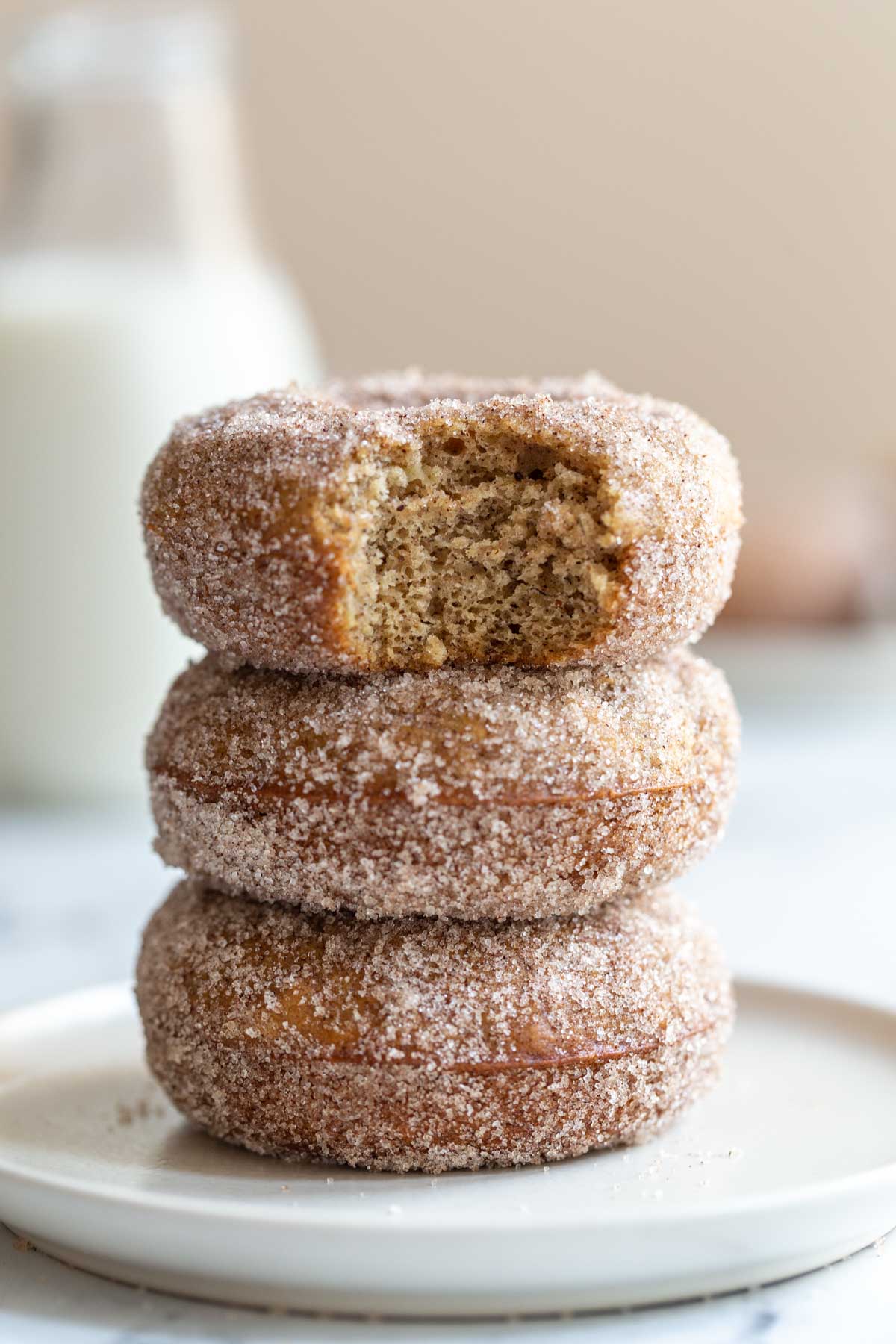 sugar coated donuts stacked up on a wood board with a bite taken out of the top donut