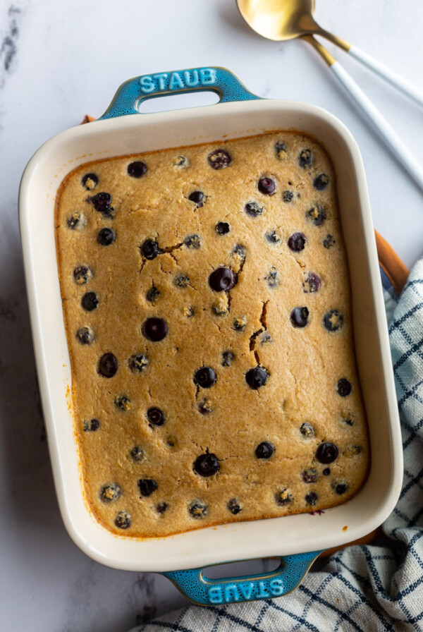 baked oats with blueberries in a small casserole dish with a napkin and spoons on the side