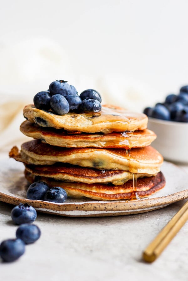 Stack of banana pancakes topped with blueberries and syrup.