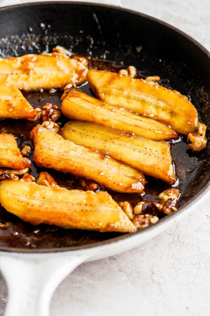 bananas cooking in a large skillet with a glaze and chopped walnuts