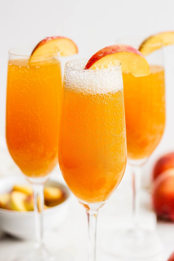 Peach bellini drinks garnished with sliced peach.