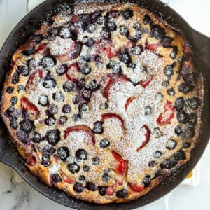 blueberry and strawberry dutch baby in a white skillet and dusted with powdered sugar