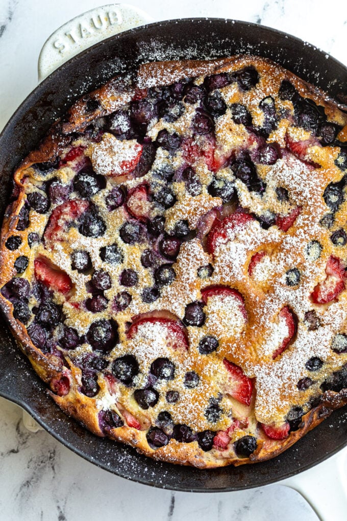 blueberry and strawberry dutch baby in a white skillet and dusted with powdered sugar