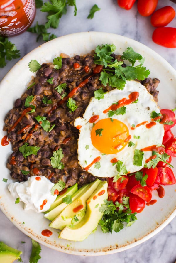 mashed blck beans on a plate with a fried egg and veggies