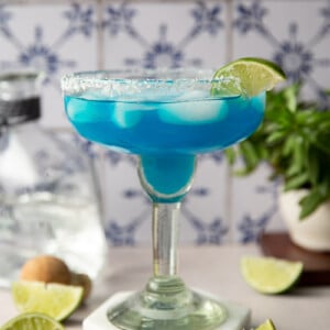 Blue margarita served with lime slices.