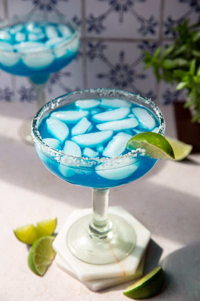 Blue cocktail with a salted rim and lime wedges.