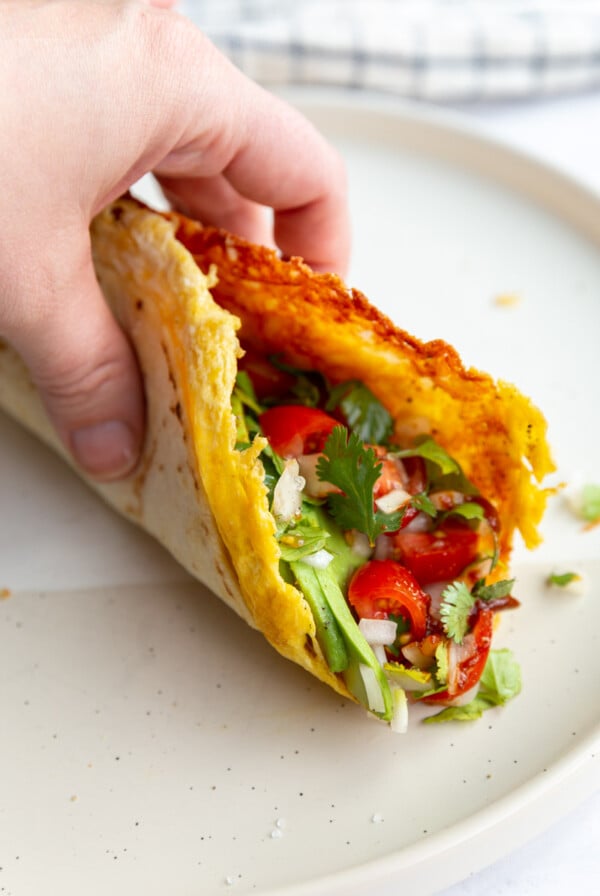 hand holding up a breakfast taco with lots of veggies in it