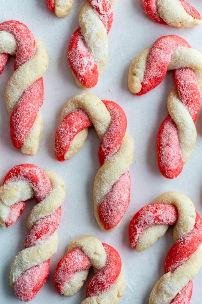 red and white sugar cookies that are twisted to look like candy canes. All laying on parchment paper