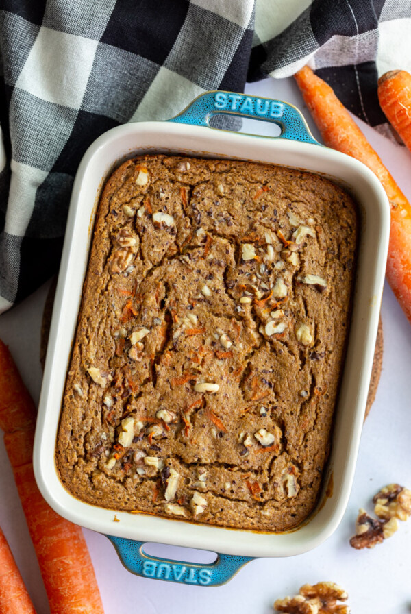 green casserole dish filled with baked carrot cake oatmeal. carrots and a towel on the side