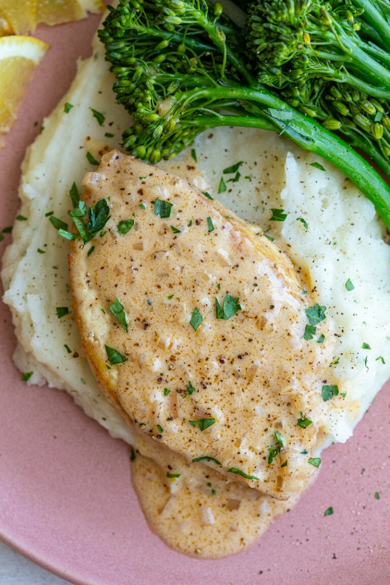 tofu slice cut in the shape of a chicken breast and topped with a chardonnay creamy sauce. The tofu is laying on top of a bed of mashed potatoes with broccolini on the side and lemon slices in the corner of the plate