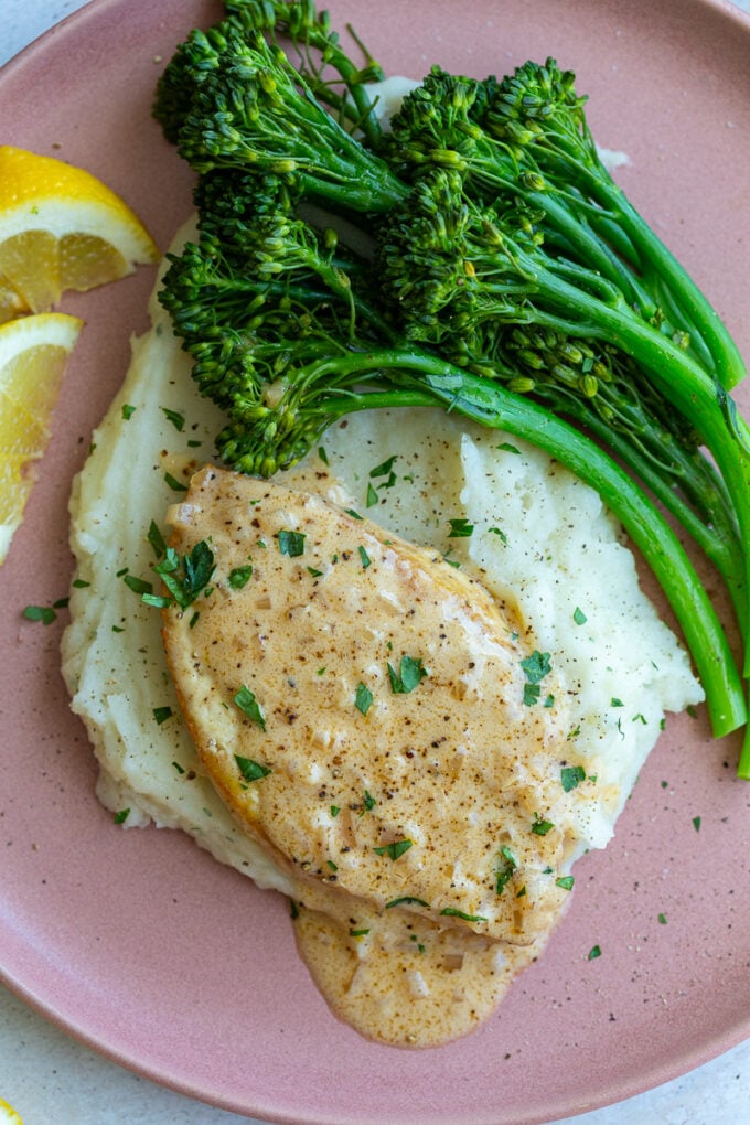 tofu slice cut in the shape of a chicken breast and topped with a chardonnay creamy sauce. The tofu is laying on top of a bed of mashed potatoes with broccolini on the side and lemon slices in the corner of the plate