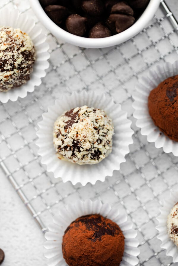 chocolate truffles covered in nuts and sitting in a mini muffin liner with more truffles around