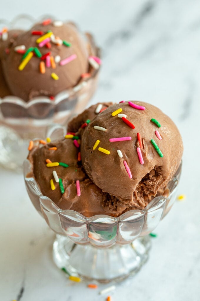 chocolate ice cream in a clear dish and topped with colorful sprinkles