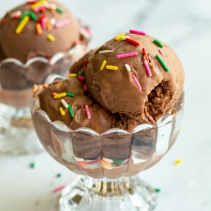 chocolate ice cream in a clear dish and topped with colorful sprinkles