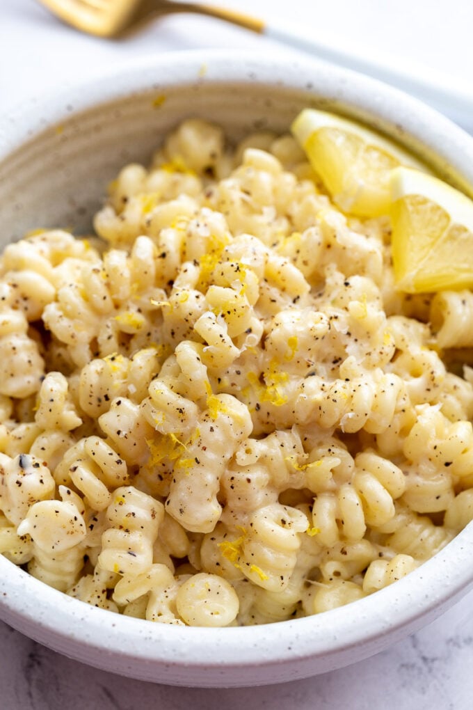 Creamy lemon pasta served with lemon wedges in a white bowl.