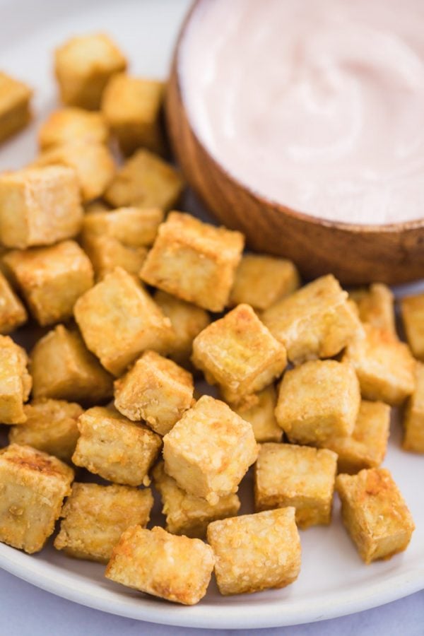 side shot of crispy tofu cubes pilled up on a white plate