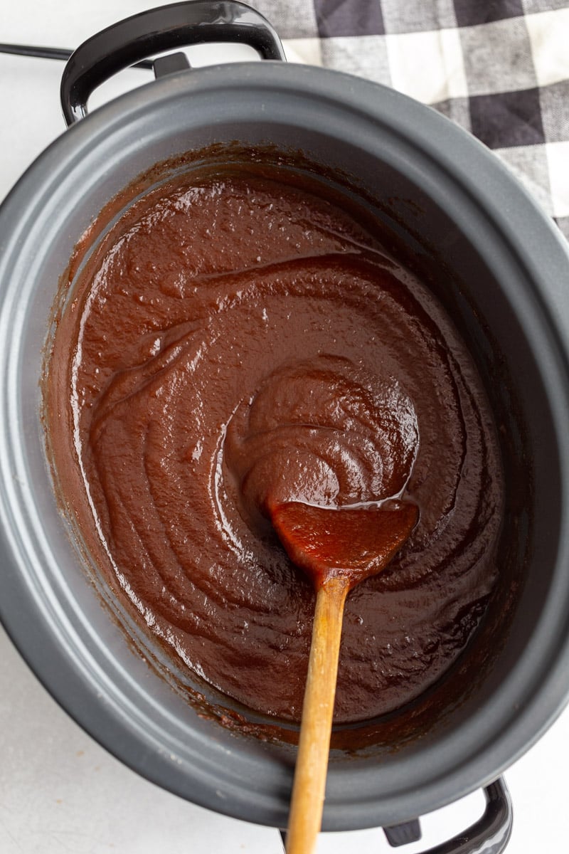 blended and smooth apple butter in a crockpot with a wooden spoon on the side