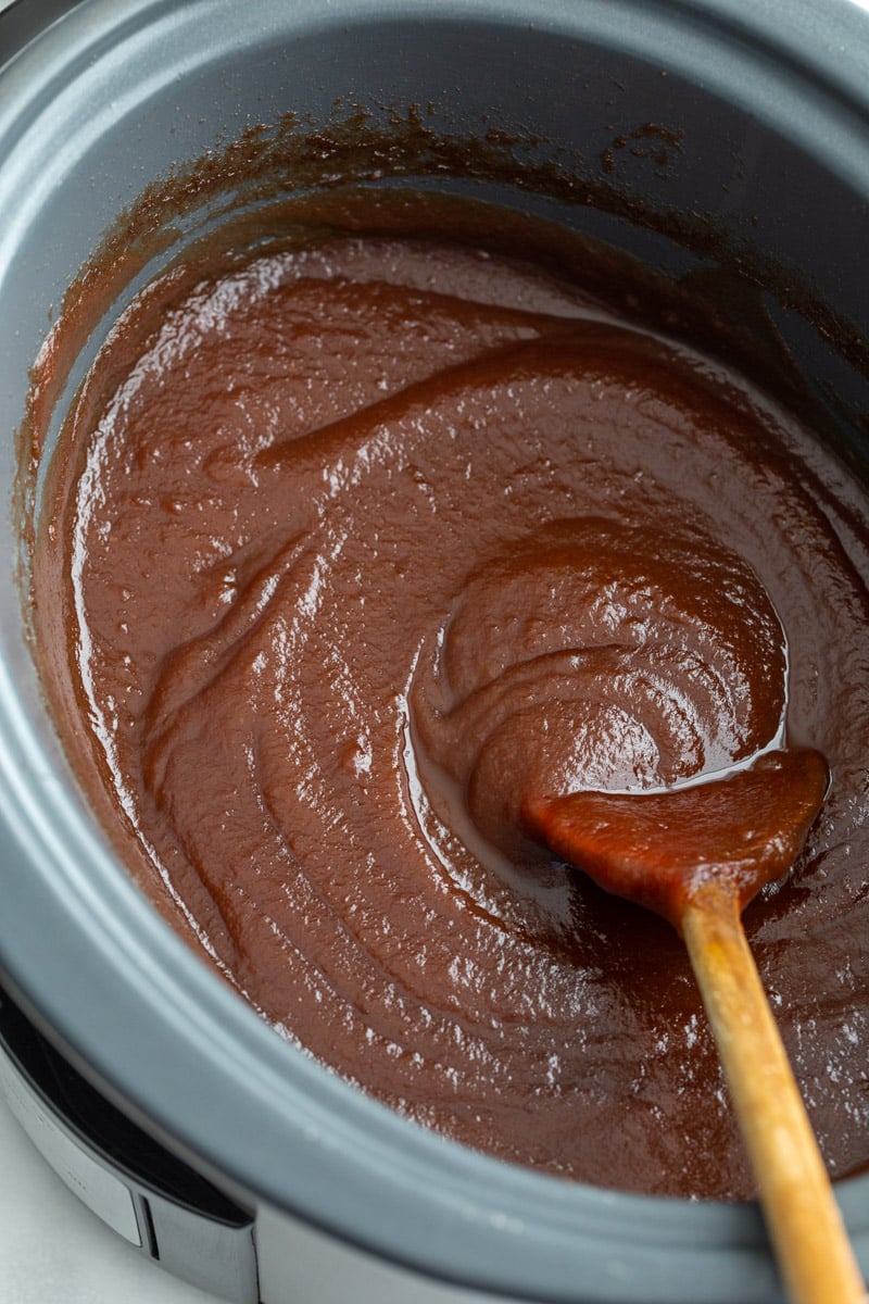 apple butter in a crockpot with a wooden spoon in the side