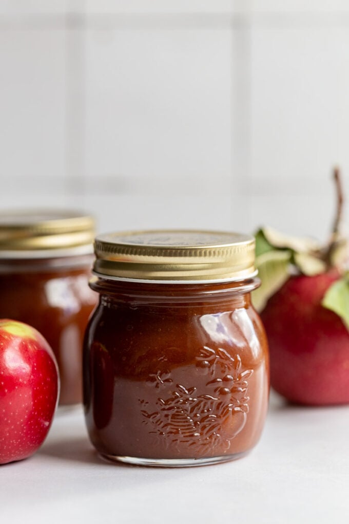 apple butter in a small jar with a golden lid and apples in the background