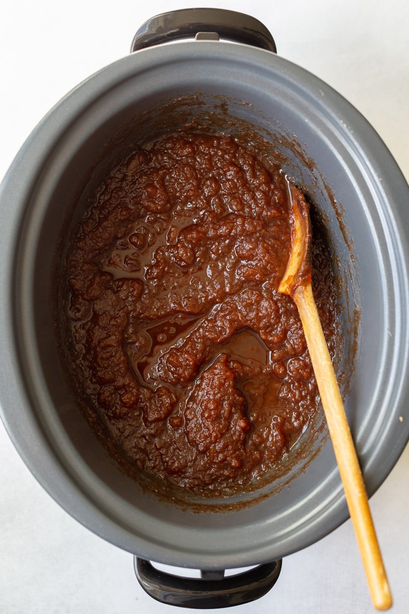 unblended apple butter in a crockpot with a wooden spoon on the side