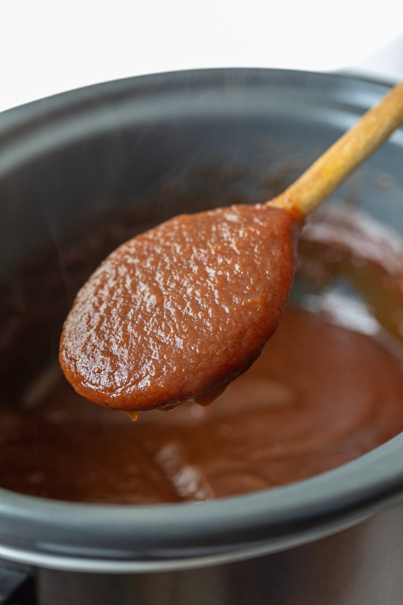 apple butter in a slow cooker with a spoonful being held up to the camera