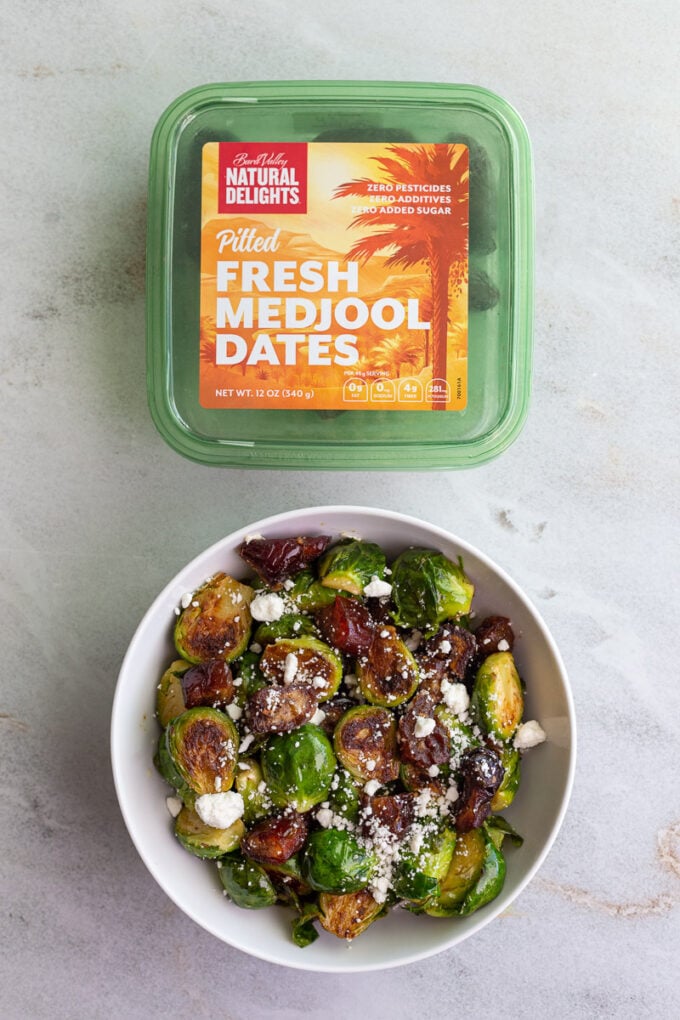 box of natural delights pitted medjool dates next to a bowl of brussels sprouts and chopped dates topped with crumbled goat cheese