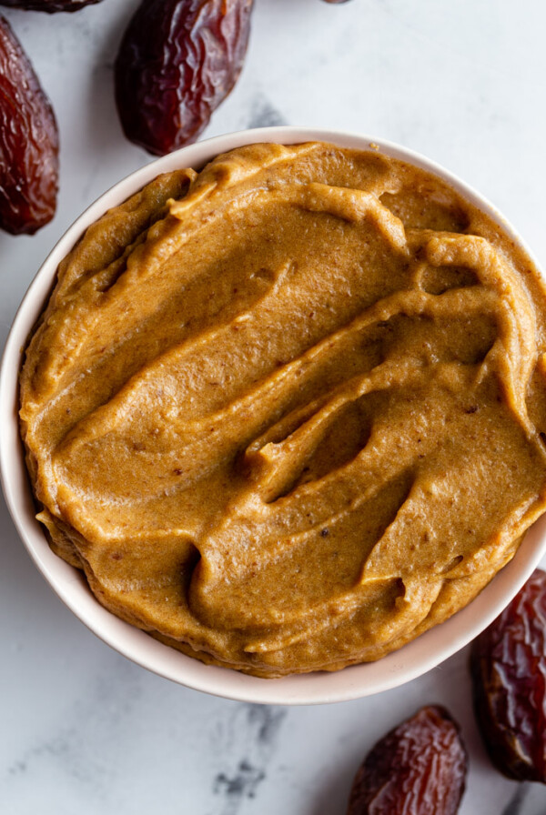 creamy date paste in a small bowl with fresh dates around the bowl