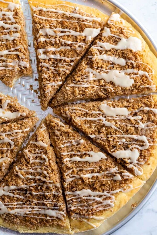 cinnamon sugar dessert pizza cut in slices and topped with a frosting. a bite is taken out of one slice