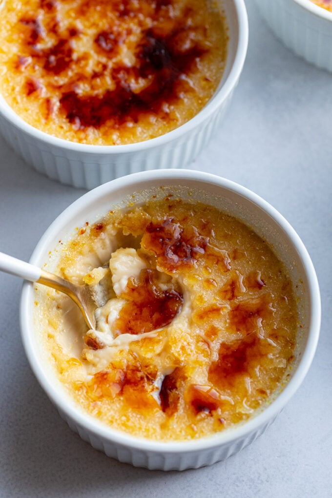 Spooning out a bite of Creme Brulee from a white ramekin.