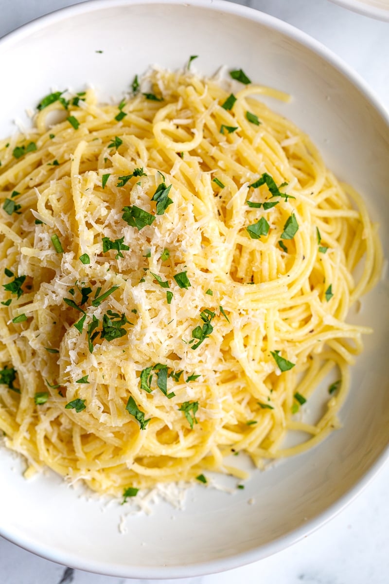 garlic butter noodles in a white bowl topped with parmesan cheese and parsley