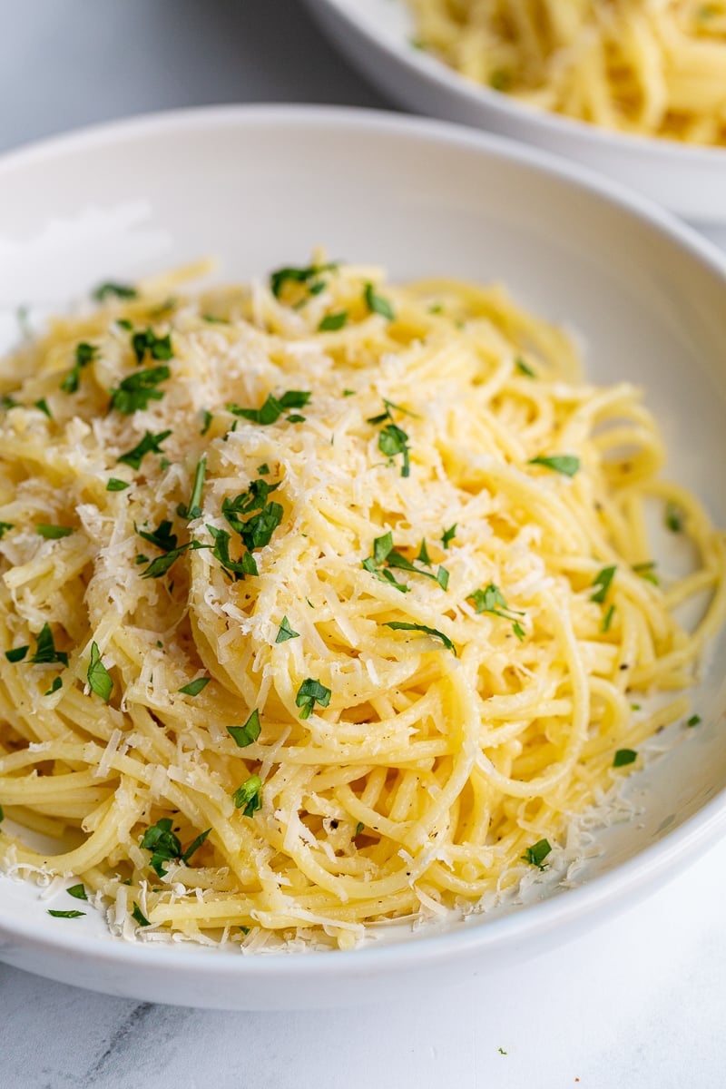 garlic butter noodles in a white bowl topped with parmesan cheese and parsley