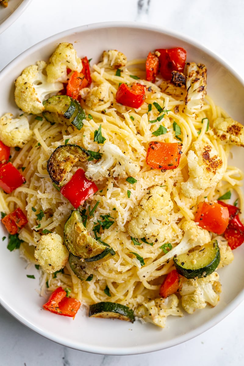 garlic butter noodles in a white bowl topped with parmesan cheese and parsley as well as roasted cauliflower, zucchini and bell pepper