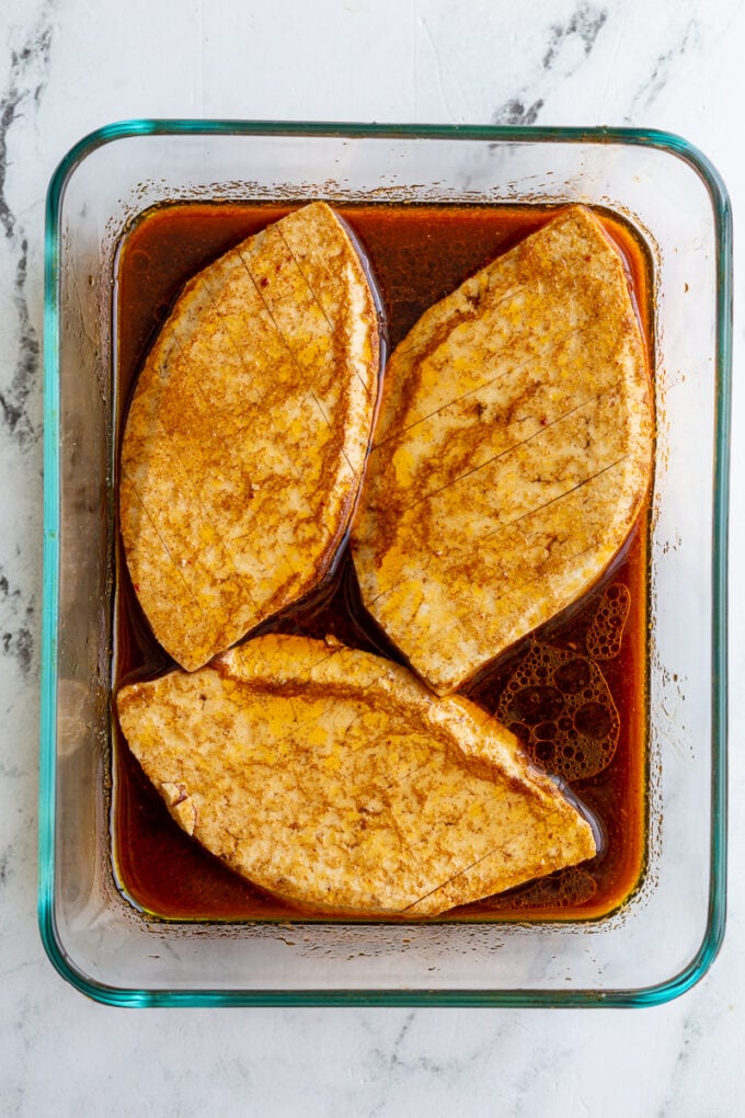 3 pieces of tofu cut to lok like chicken breast sitting in a container with marinade