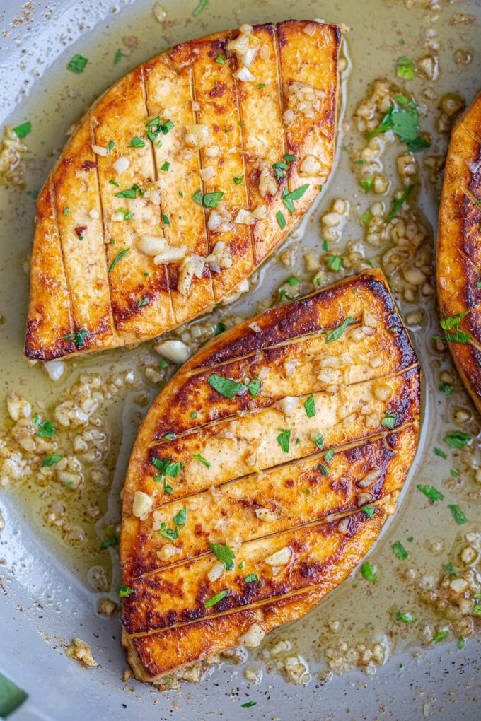 tofu "steaks" in a skillet with garlic butter and fresh green herbs