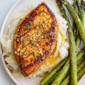 garlic butter tofu that loks a lot like a chicken breasts sitting on top of mashed potatoes with roasted asparagus on he side of the plate