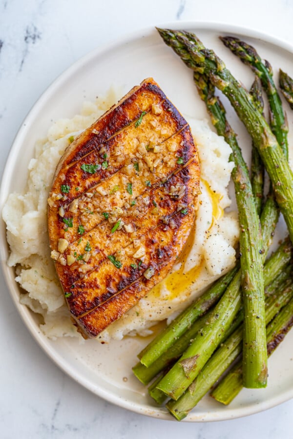 garlic butter tofu that loks a lot like a chicken breasts sitting on top of mashed potatoes with roasted asparagus on he side of the plate