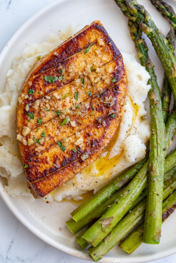 garlic butter tofu that loks a lot like a chicken breasts sitting on top of mashed potatoes with roasted asparagus on he side of the plate