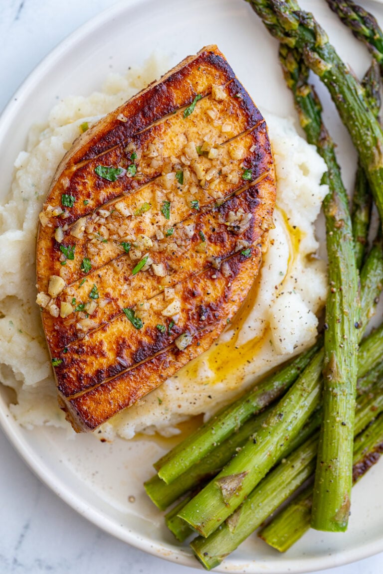 garlic butter tofu that loks a lot like a chicken breasts sitting on top of mashed potatoes with roasted asparagus on he side of the plate