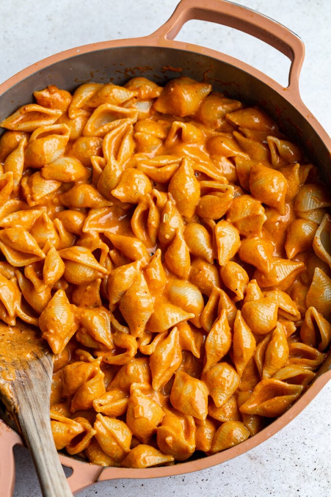 Stirring pasta and sauce in a large skillet.