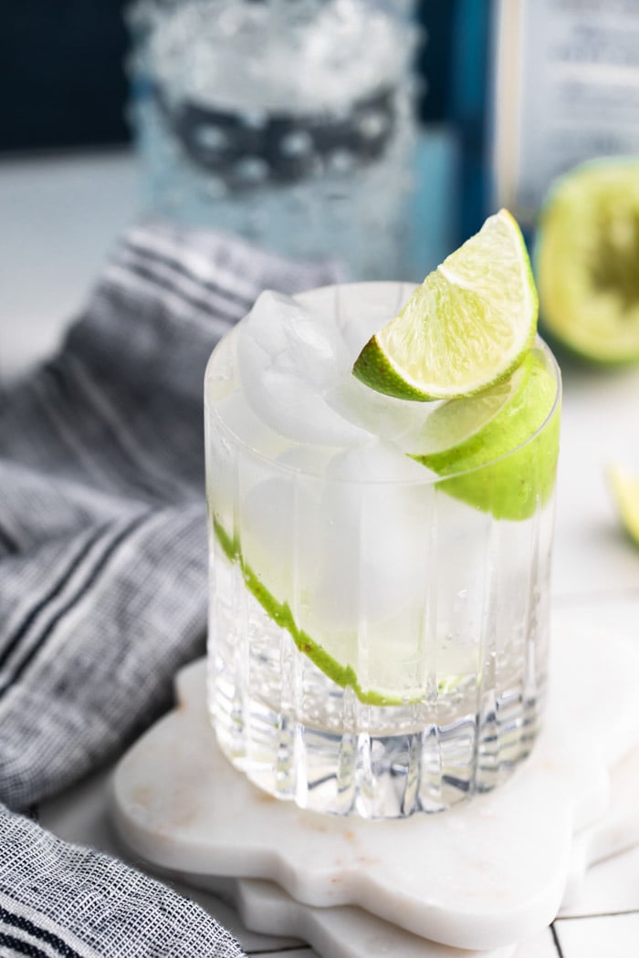 clear beveled glass filled with clear liquid (gin and tonic) plus fresh lime wedges towel on the side