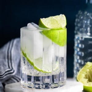 clear beveled glass filled with clear liquid (gin and tonic) plus fresh lime wedges. dark background