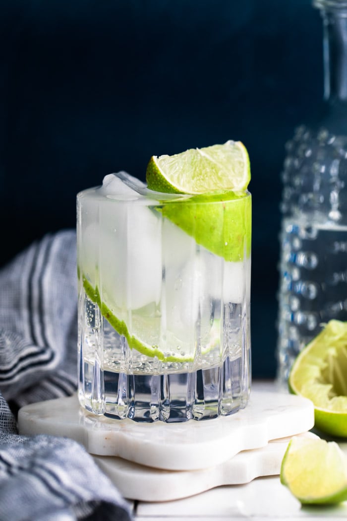 clear beveled glass filled with clear liquid (gin and tonic) plus fresh lime wedges. dark background