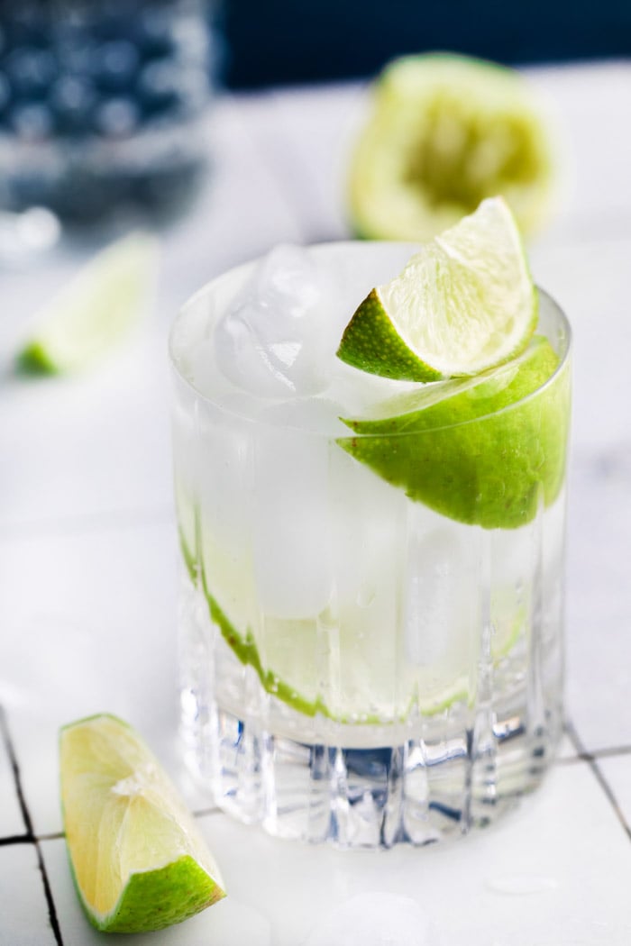 clear beveled glass filled with clear liquid (gin and tonic) plus fresh lime wedges