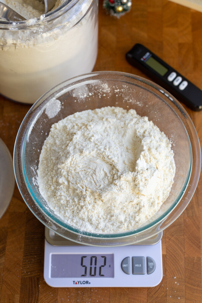 bowl of flour sitting on a kitchen scale that reads "502g". there's more flour and a kitchen thermometer in the background